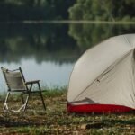 camping setup with a tent and folding chair beside a lake, illustrating the kind of outdoor scene where portable solar blankets are useful