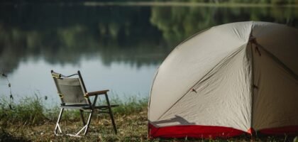 camping setup with a tent and folding chair beside a lake, illustrating the kind of outdoor scene where portable solar blankets are useful