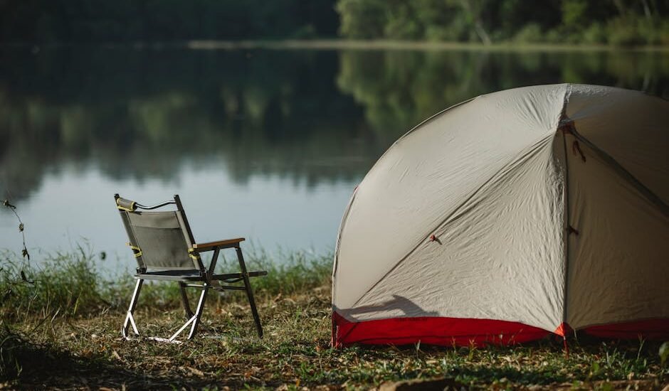 camping setup with a tent and folding chair beside a lake, illustrating the kind of outdoor scene where portable solar blankets are useful