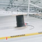 A spool of black solar extension cable sits on a metal roof beneath mounted solar panels, illustrating solar wiring setup.