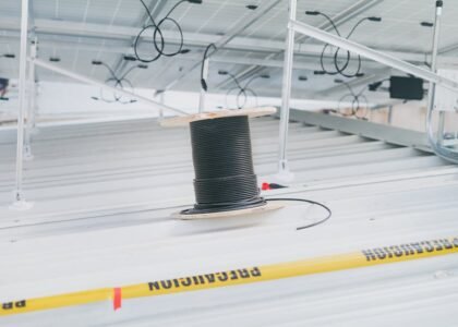 A spool of black solar extension cable sits on a metal roof beneath mounted solar panels, illustrating solar wiring setup.