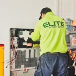 Electrician working on a wall-mounted battery bank, illustrating deep cycle battery setup for off-grid power solutions.