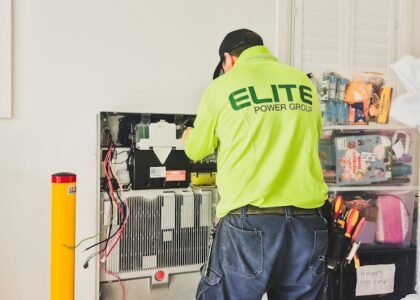 Electrician working on a wall-mounted battery bank, illustrating deep cycle battery setup for off-grid power solutions.