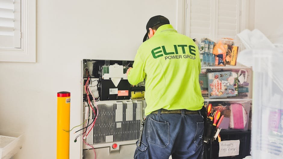 Electrician working on a wall-mounted battery bank, illustrating deep cycle battery setup for off-grid power solutions.