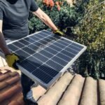 Person in gloves installing a solar panel on a tiled roof, illustrating steps in choosing a solar generator kit for home backup power.