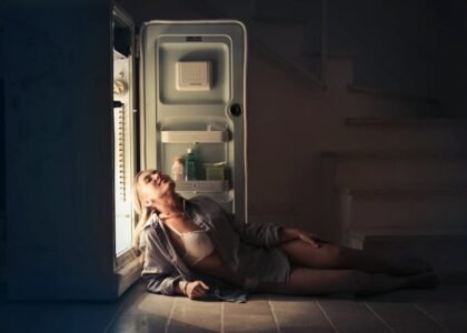 A woman sits on the floor leaning against an open fridge, illustrating real-life use and energy needs for DC vs AC fridges in off-grid living.