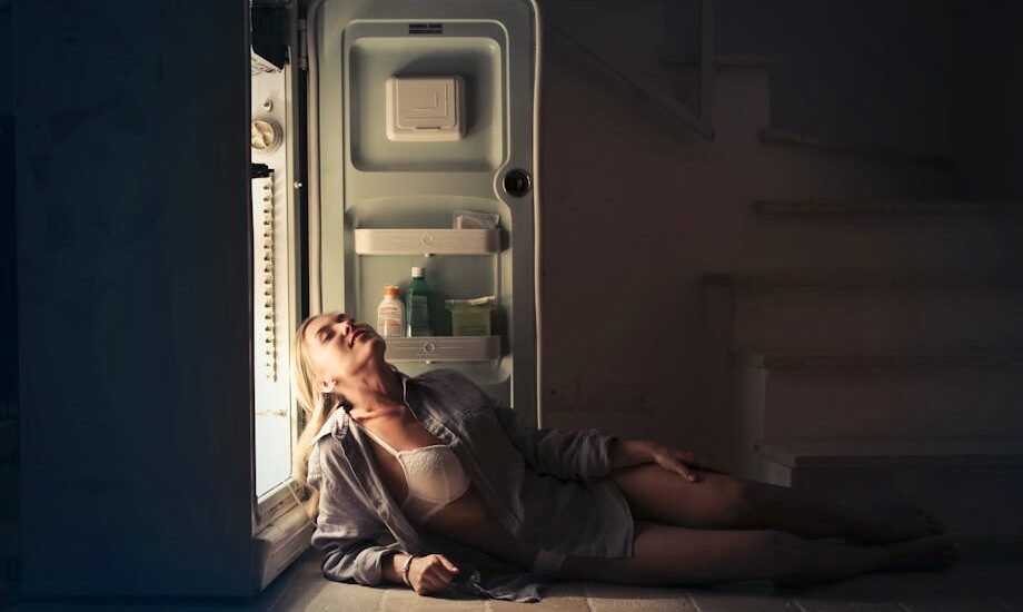 A woman sits on the floor leaning against an open fridge, illustrating real-life use and energy needs for DC vs AC fridges in off-grid living.
