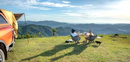 Two campers sit by a table with a portable solar blanket on the grass, overlooking mountains, for a solar blanket review article