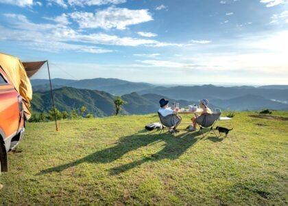 Two campers sit by a table with a portable solar blanket on the grass, overlooking mountains, for a solar blanket review article