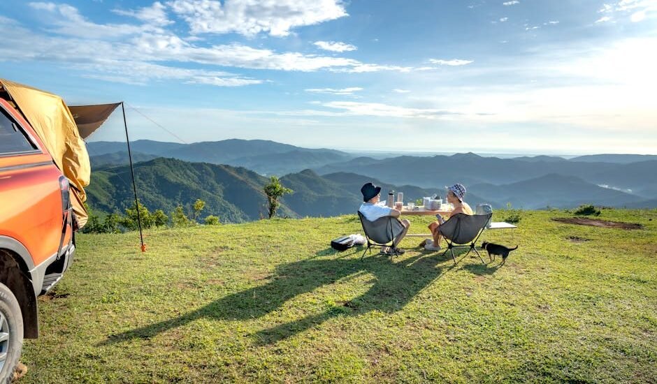 Two campers sit by a table with a portable solar blanket on the grass, overlooking mountains, for a solar blanket review article