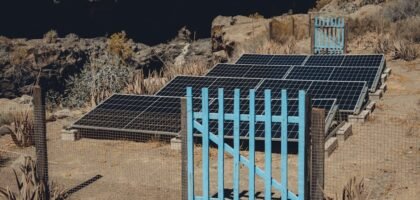 Solar charge controller functions illustrated by ground-mounted solar panels behind a blue gate in a dry, rocky area