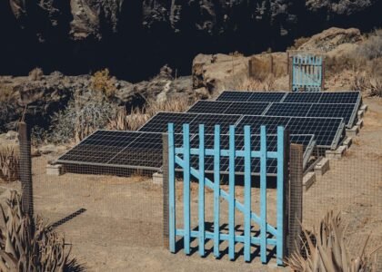 Solar charge controller functions illustrated by ground-mounted solar panels behind a blue gate in a dry, rocky area