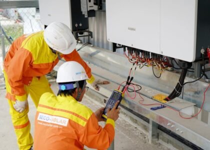 Two technicians in safety gear test a large solar string inverter, illustrating the differences between string and micro inverters.