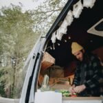 Person preparing food inside a camper van kitchen, illustrating van life and the use of 12V refrigerators for off-grid living.
