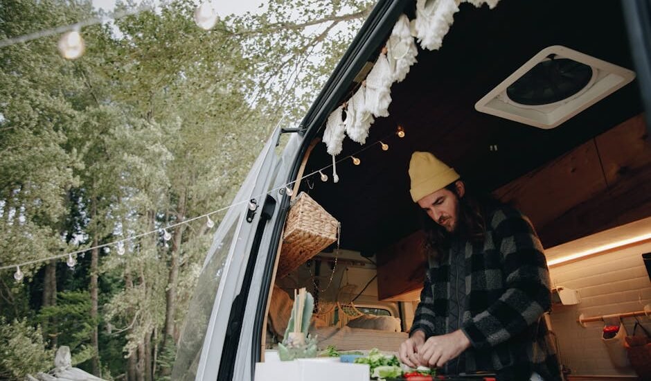 Person preparing food inside a camper van kitchen, illustrating van life and the use of 12V refrigerators for off-grid living.