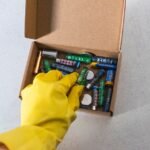 A hand in a yellow glove reaching for various batteries in a box, illustrating battery depth of discharge concepts.