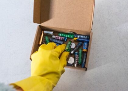 A hand in a yellow glove reaching for various batteries in a box, illustrating battery depth of discharge concepts.