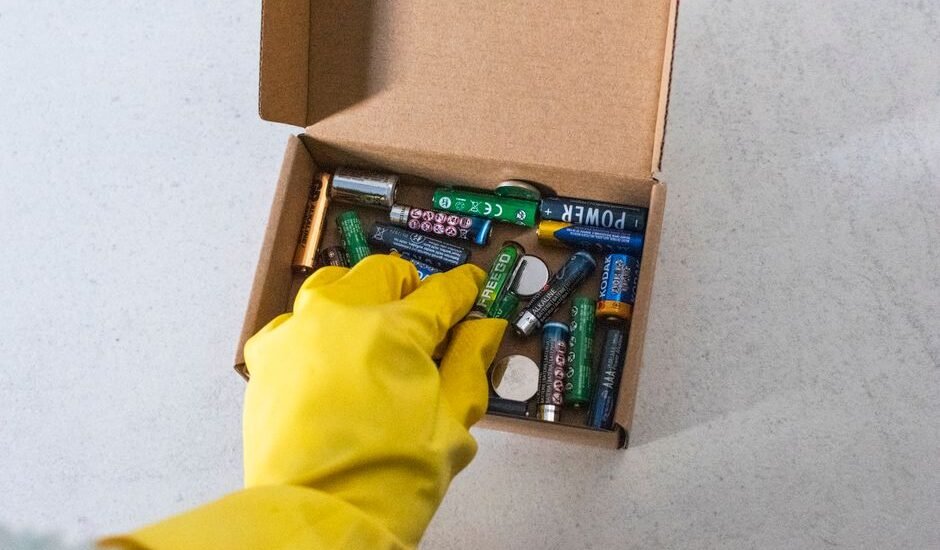 A hand in a yellow glove reaching for various batteries in a box, illustrating battery depth of discharge concepts.