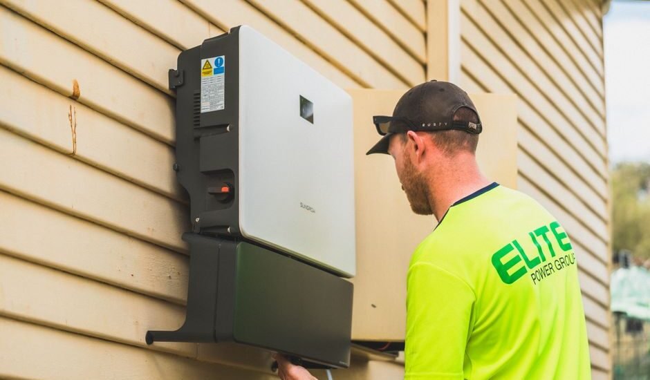 A technician installs an all-in-one inverter charger on a wall, relevant to inverter charger buying guide.