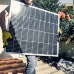 A person in gloves carrying a solar panel, relevant to solar battery maintainers.