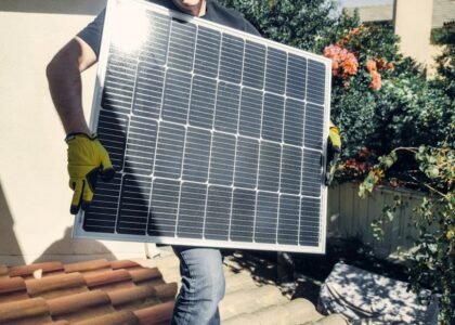 A person in gloves carrying a solar panel, relevant to solar battery maintainers.
