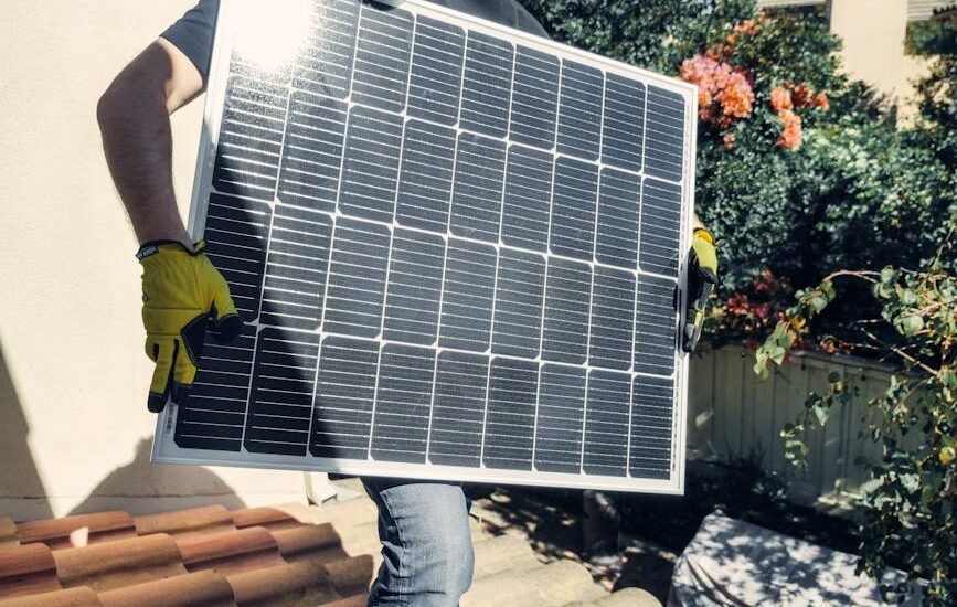 A person in gloves carrying a solar panel, relevant to solar battery maintainers.