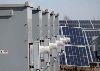 A row of solar combiner boxes next to solar panels, illustrating solar power setup.