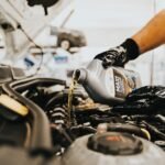 A person pours oil into a generator's engine, illustrating oil change frequency.