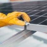 A person in a green shirt and yellow gloves secures a solar panel, relevant to lead acid vs gel batteries.