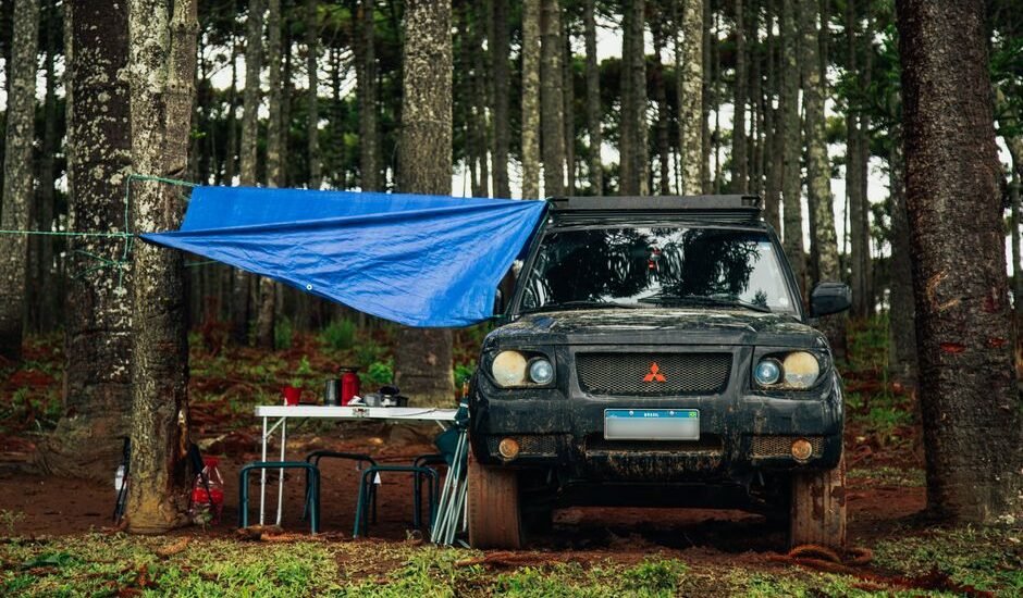 A vehicle with a tarp setup in a forest, illustrating off-grid living options like power stations and batteries.