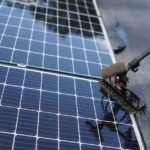 A person using a brush to clean solar panels, illustrating effective cleaning techniques.