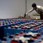 A person inspecting numerous blue batteries, illustrating the charge efficiency factor in energy storage.