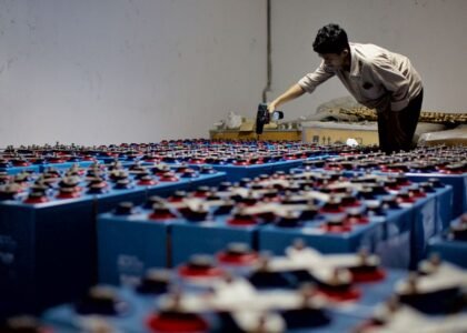 A person inspecting numerous blue batteries, illustrating the charge efficiency factor in energy storage.