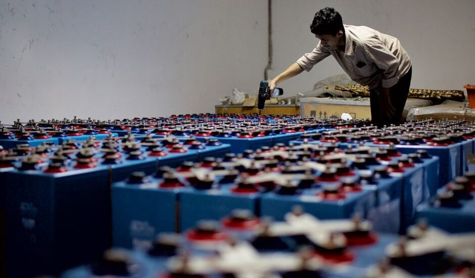 A person inspecting numerous blue batteries, illustrating the charge efficiency factor in energy storage.