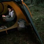 A person inside a tent using a laptop, illustrating the convenience of portable power stations for outdoor activities.