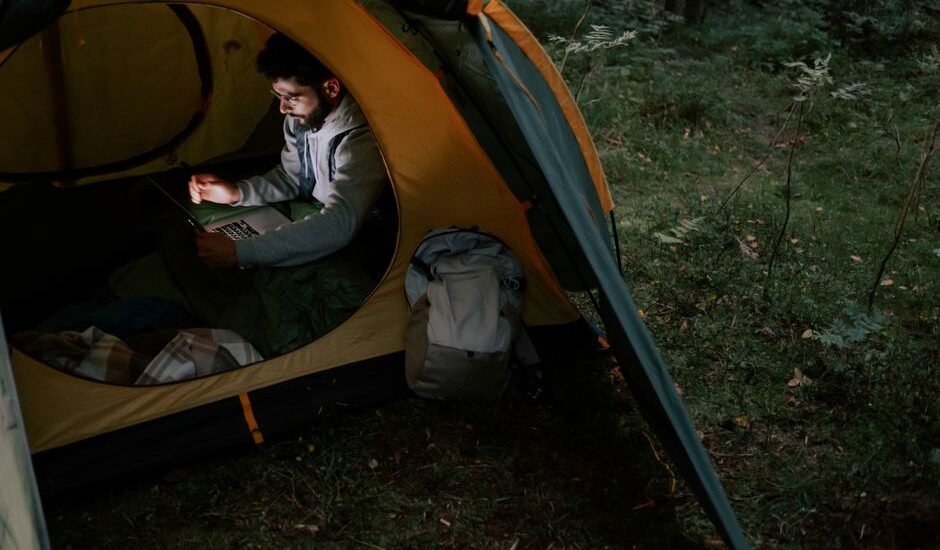 A person inside a tent using a laptop, illustrating the convenience of portable power stations for outdoor activities.